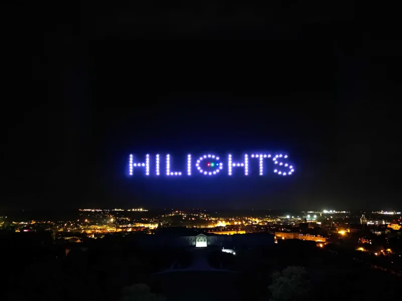 Logo HILIGHTS dessiné dans le ciel par une flotte de drones lumineux au-dessus d'une ville la nuit