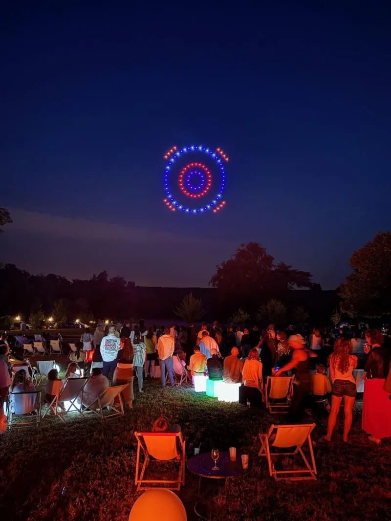 Cercles concentriques bleus et rouges dessinés par les drones, invités installés en transats