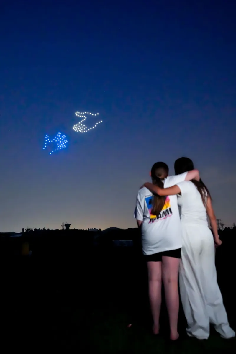 Deux spectatrices enlacées devant un spectacle de drones lumineux