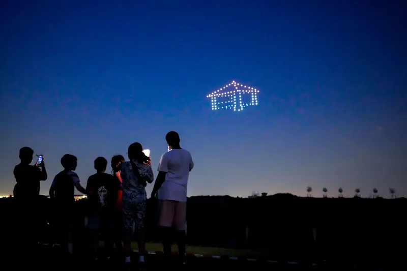 Maison dessinée en drones lumineux, des enfants et des parents regardent le ciel
