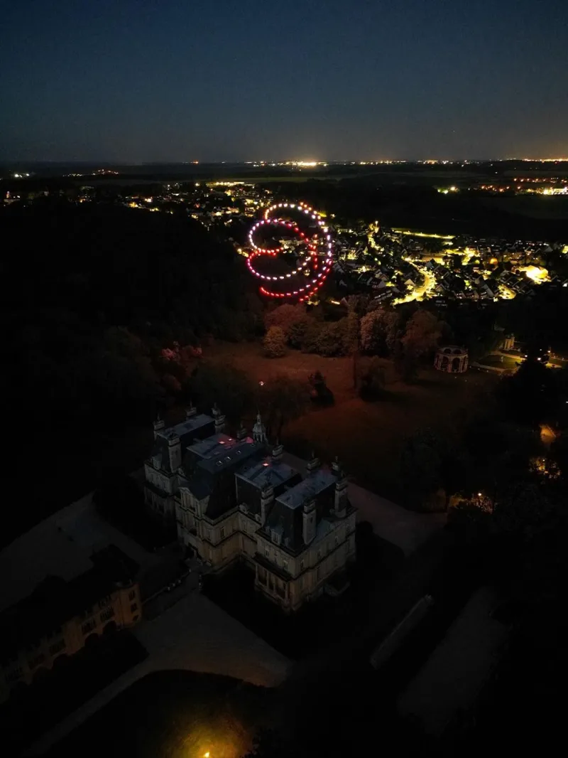 Spirale rouge de drones lumineux au-dessus d'un château et d'une ville la nuit