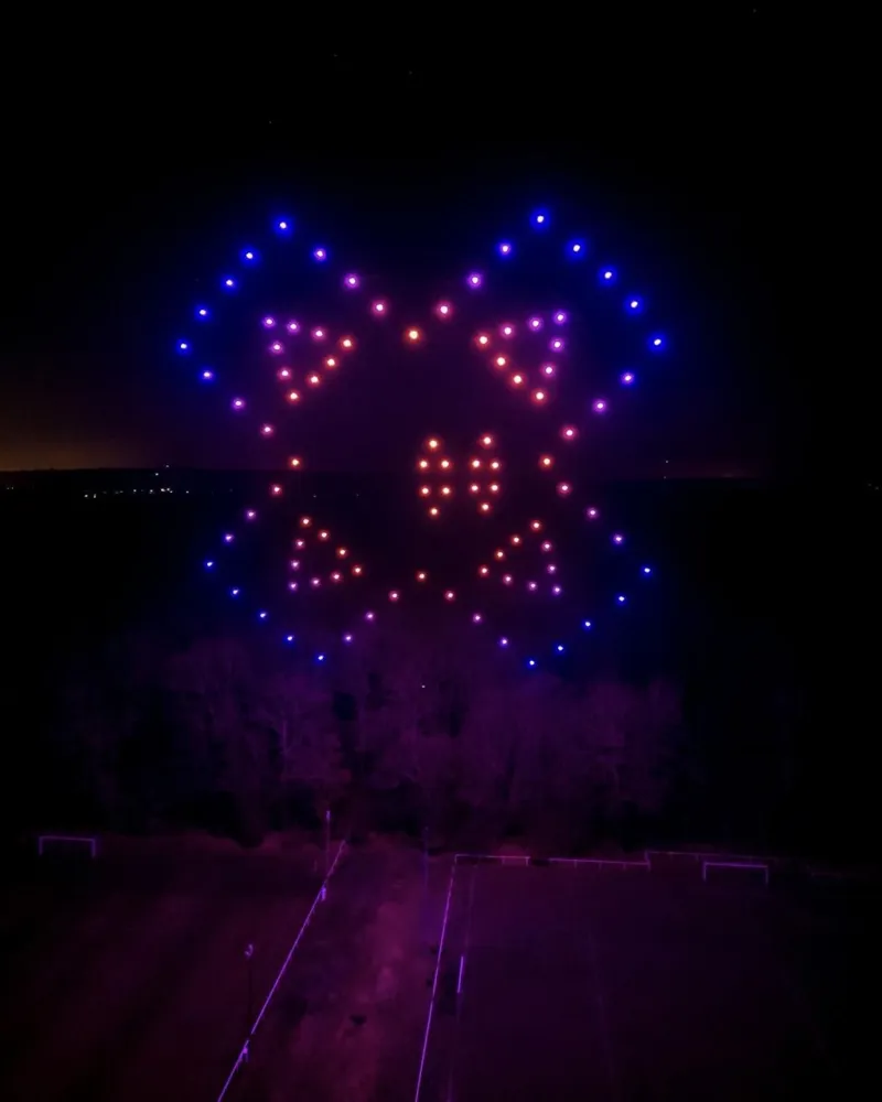 Figure symétrique en drones lumineux roses et bleus au-dessus d'un terrain