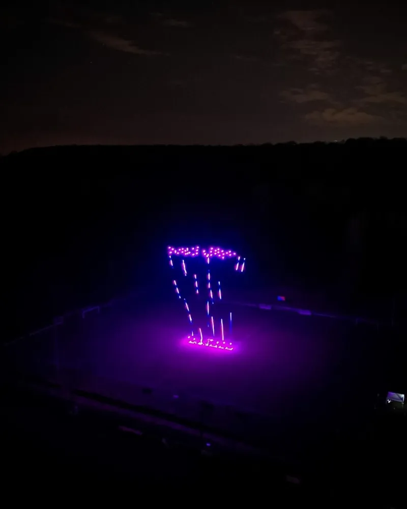 Figure violette en drones lumineux au-dessus d'un terrain de répétition