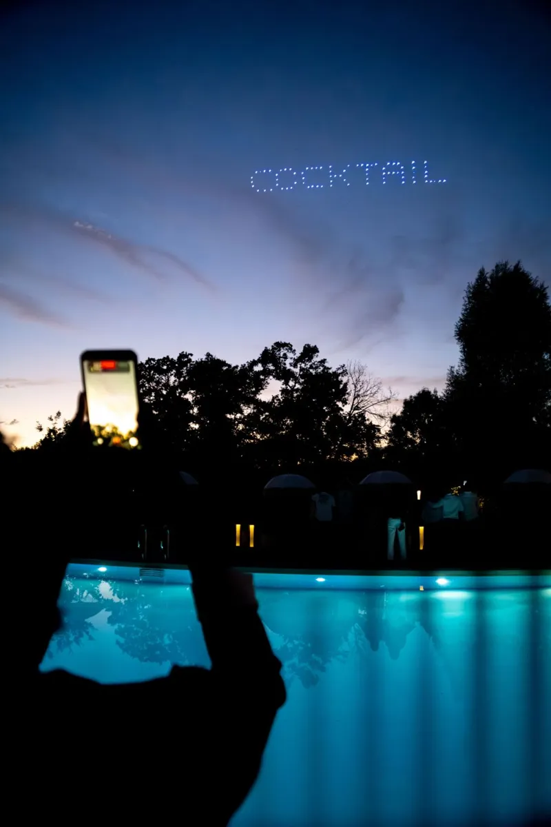 Mot « COCKTAIL » écrit en drones lumineux au-dessus de la piscine